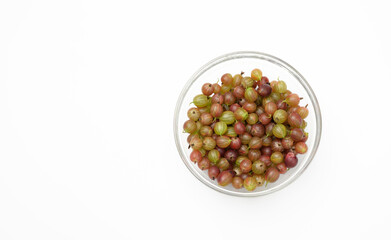 ripe green and red gooseberries in a transparent glass bowl on a white background