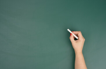 hand holds a piece of white chalk on the background of an empty green chalk board, presentation concept