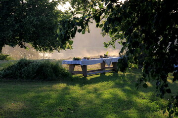 Outdoors summer scene party table on sunset. Old wooden table under trees with food plate. Midsummer celebrating in Latvia, Ligo festive