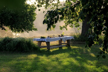 Outdoors summer scene party table on sunset. Old wooden table under trees with food plate. Midsummer celebrating in Latvia, Ligo festive