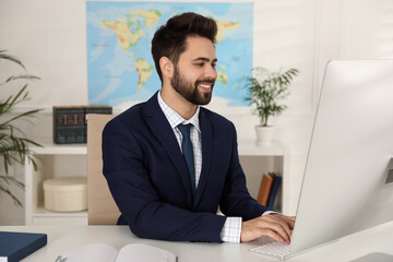 Naklejka premium Happy manager working with computer at desk in travel agency