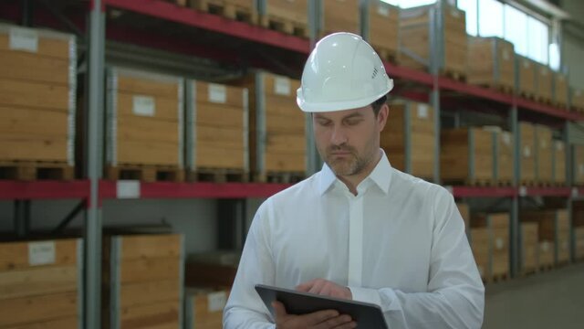 Employee male warehouse worker engineer man in hard hat working at construction site warehouse, walking in logistics center factory, storekeeper using tablet computer, architect businessman indoors