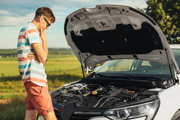 Concentrated young man holding on to the hood of a car and looking inside while standing , Breakdown of the car