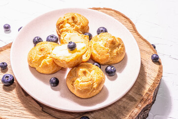 Profiteroles with blueberries. Custard cakes, Eclair, cream puff on a wooden stand