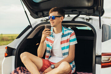 Male traveler enjoying coffee in the back storage of a car with panoramic view of beautiful nature, travel concept