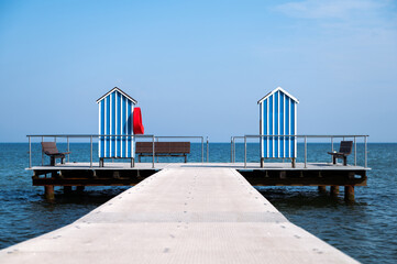 Fototapeta premium End of pier with two wooden houses as changing room and benches on blue sky background