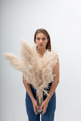 portrait of young caucasian woman with long hair in blue jeans holding bouquet of pampas grass on...