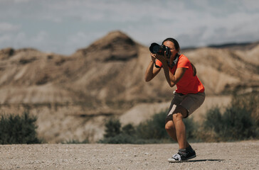 Woman photographer in action taking photos in Tabernas Desert, Spain, in a sunny day, with an orange color t-shirt.