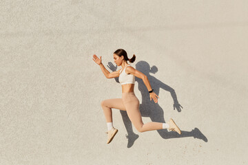 Portrait of woman with perfect body jumping over in the air, wearing white top and beige leggins,...