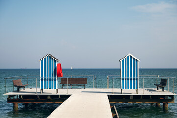 End of pier with two wooden houses as changing room and benches on blue sky background