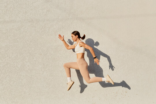 Portrait Of Woman With Perfect Body Jumping Over In The Air, Wearing White Top And Beige Leggins, Doing Sports Exercises Outdoor, Healthy Lifestyle, Body Care.