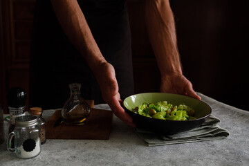 a man prepares a vegetable salad on a dark background. Dark photo style. Demonstration of the finished salad