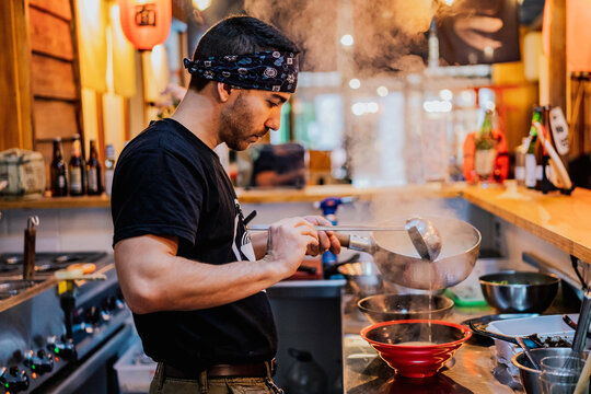 Man in bandana standing at counter and cooking ramen