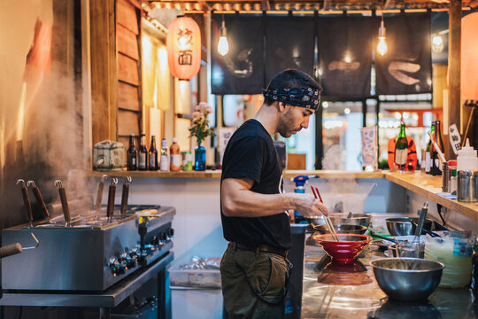 Man in bandana standing at counter and cooking ramen