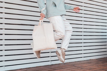 Young woman jumping with white cotton bag in her hands. Mockup and zero waste concept.