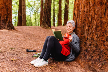 Elderly woman relaxes having a cup of coffee and reading a book in the forest. activities for the elderly.