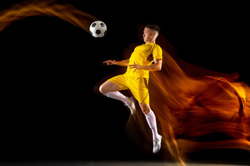 Fototapeta premium Young caucasian male football or soccer player training in mixed light isolated on dark background. Concept of healthy lifestyle, professional sport, active, motion..