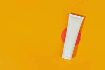 Flat lay top view blank white tube bottle with lotion cream or cleanser on orange background