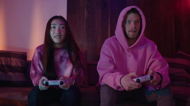 Girl and boy playing console video games together sitting on sofa with neon lights. Smiling, video games, playstation, entertainment, internet, controller. Slow motion
