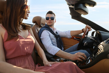 Stylish couple driving luxury convertible car outdoors