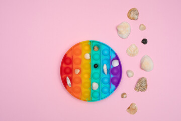 Fototapeta na wymiar antistress toy pop it round shape with sea shells, stones on pink background