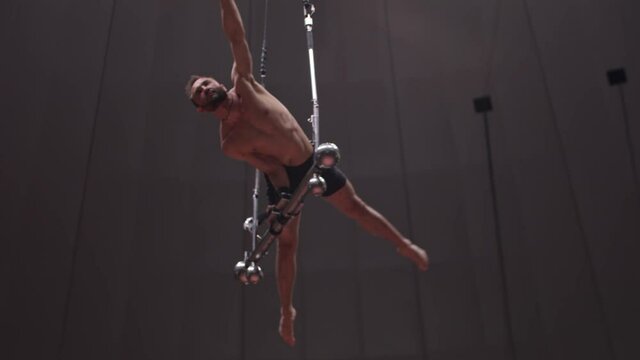 Acrobatic bearded man standing on hands on performance construction at the circus arena 