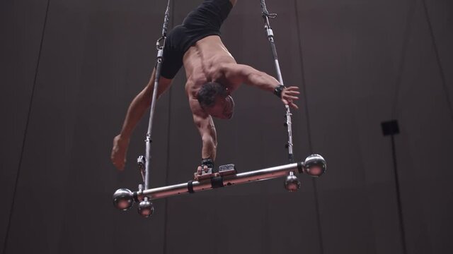 Acrobatic man training at the circus arena - standing upside down on performance construction 