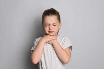 Little girl suffering from sore throat on grey background