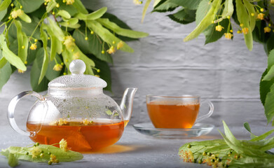 Teapot and cup with linden tea and flowers on a wooden table against a brick wall background