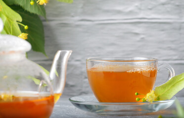 Teapot and cup with linden tea and flowers on a wooden table against a brick wall background