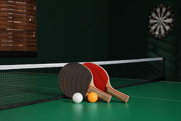 Rackets and balls on green ping pong table indoors. Space for text