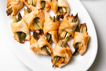 top view of tasty roasted asparagus wrapped in french pastry on white plate.