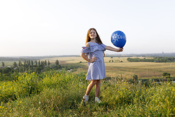 Naklejka premium happy girl with red hair and blue dress having fun with an balloon in nature