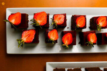 top view portions of chocolate brownie with strawberries on white plate.