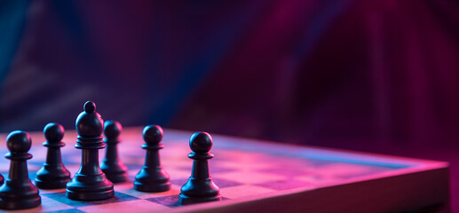 Chess pieces on a chessboard on a dark background shot in neon pink-blue colors. The figure of a...