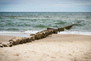 Landscape of beach and wooden breakwaters with sea waves. Stormy day at sea