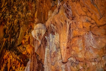Fototapeta na wymiar Brown stone mineral formations on the wall in Damlatas cave in Alanya (Turkey), close-up. Natural abstract brown-orange background of stalactites and stalagmites