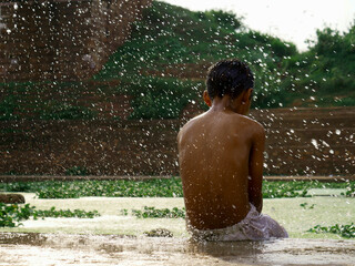 Little boy bathing with enjoyment at river bank, water drops presented all frame natural background