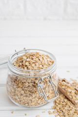 Raw dry oatmeal flakes in a glass jar on a white wooden background. Healthy food. Copy space.