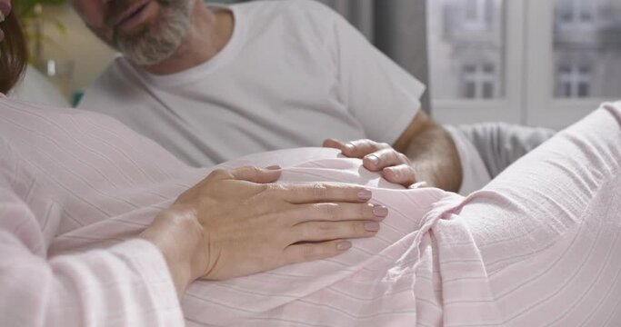 Close up view of the bearded man stroking with the hand stomach of his pregnant wife and feeling happy while waiting for a baby. Family concept
