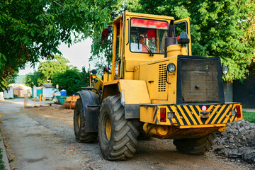Yellow tractor rides down the street against the backdrop of construction work. Road works involving a yellow tractor.