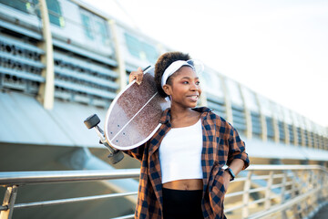 Portrait of happy african-american woman with skateboard. Young stylish woman with skateboard...