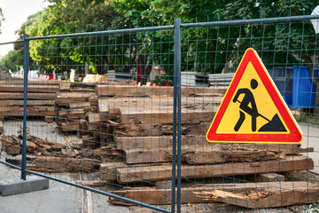 Sign of construction work on the background of wooden sleepers. Construction work to replace streetcar tracks in the city. Sign of road works installed on the construction fence in the daytime.