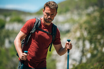 Male hiker walking with trekking poles in mountainous terrain