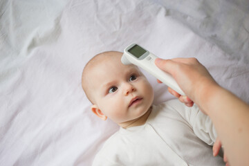 Fever and colds in an infant runny nose, flu or covid.Mom's hand holds a thermometer at the child's forehead and measures his temperature..