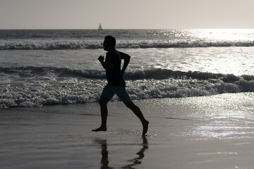 athletic man runner silhouette run on summer beach with sea water and sun, motivation