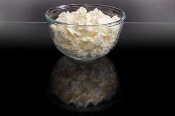 Cottage cheese in glass bowl on a dark reflective surface