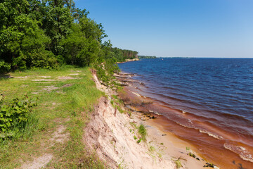 Steep shore of big reservoir overgrown with forest in summer
