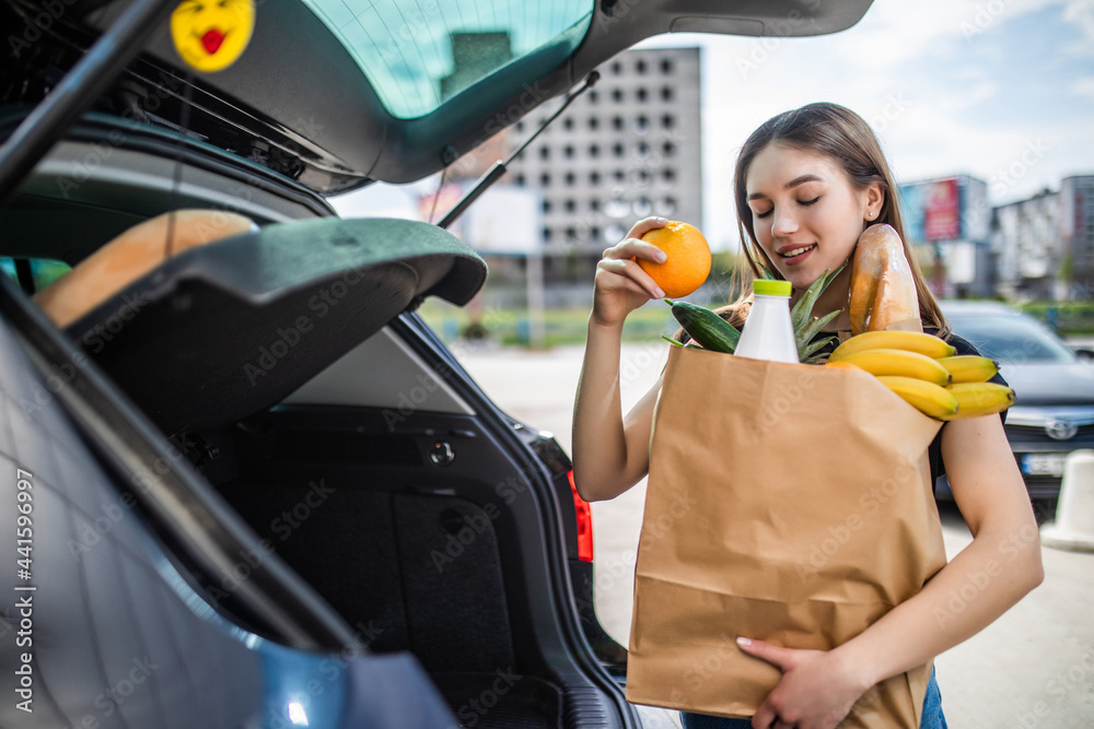 Wall mural a process of young attractive woman taking groceries from a supermarket from the trolley to car truc