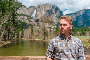 Young blonde man in Yosemite National Park with a view of a waterfall in the mountains